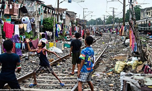 Lũ trẻ chơi bóng trên đường ray ở thành phố Kolkata, bang Tây Bengal, Ấn Độ trong khi một đoàn tàu hỏa lướt qua. Những ngôi nhà lụp xụp ở  khu nhà ổ chuột gần đường tàu phân bố trên khu vực có chiều dài khoảng 3 km.